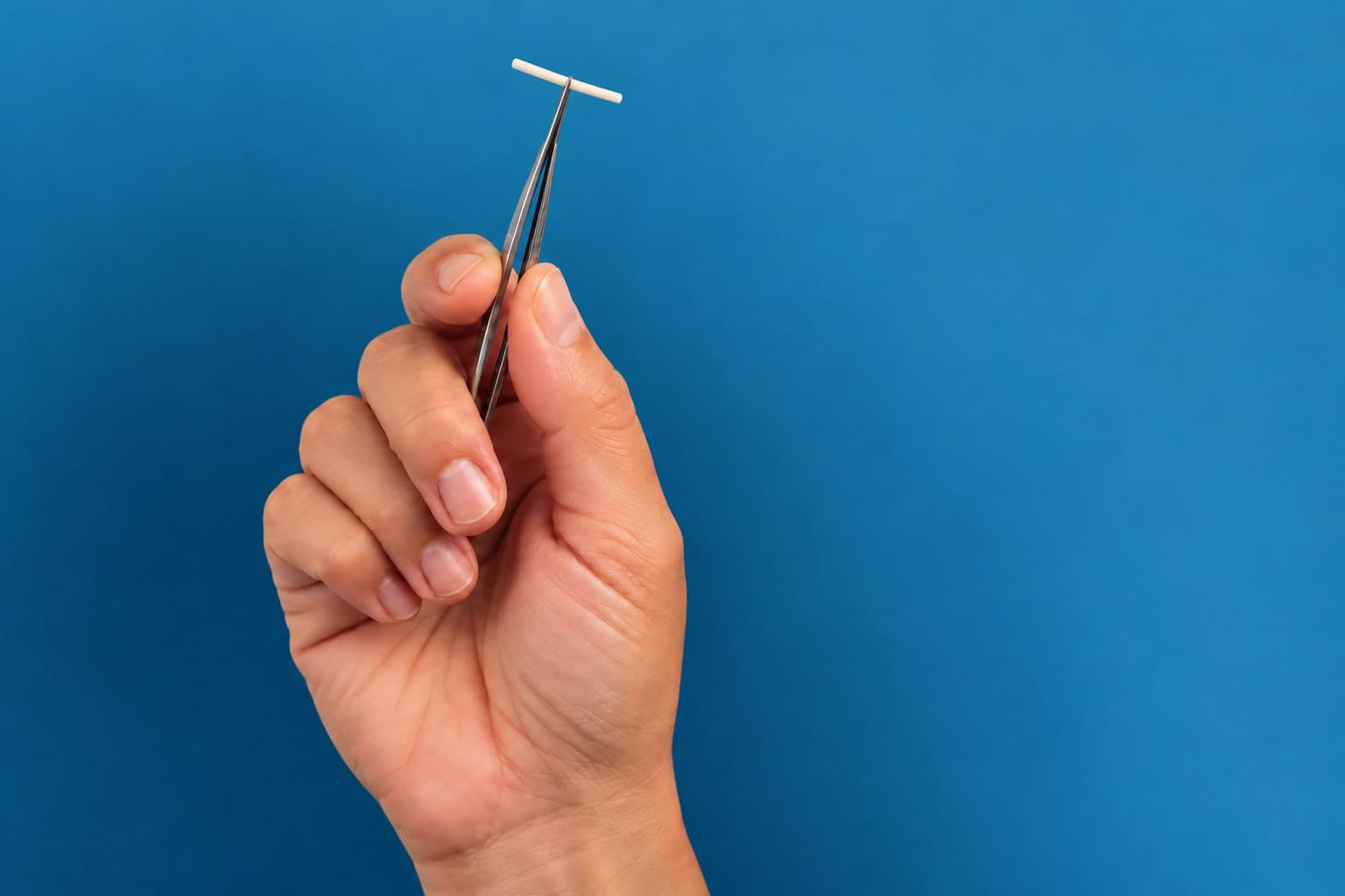 A birth control implant, about the size of a matchstick, held in tweezers